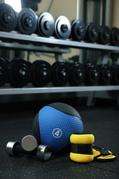 Blue medicine ball, weighting agents and dumbbells on floor in gym, space for text