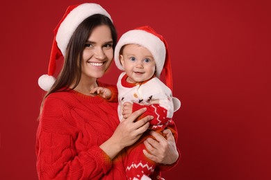Happy mother with cute baby in Christmas outfits and Santa hats on red background