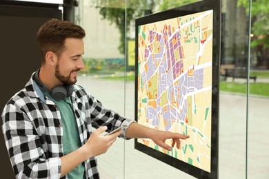 Young man with smartphone near public transport map at bus stop