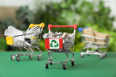 Photo of Shopping cart with recycling symbol full of garbage on green table