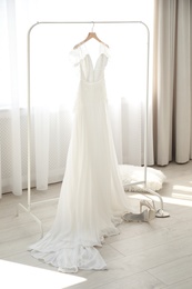 Beautiful wedding dress hanging on clothing rack in room