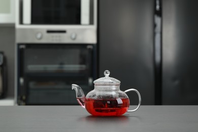 Photo of Glass teapot with delicious tea on grey table in kitchen