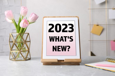 Image of Future trends. 2023 What's New? text on tablet display. Modern gadget, flowers and stationery on table
