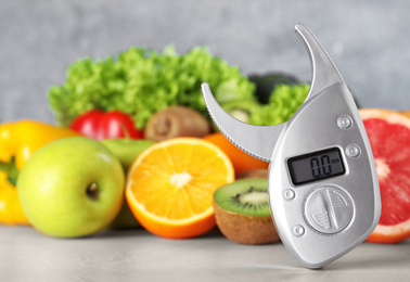 Digital body fat caliper, vegetables and fruits on table. Diet plan from nutritionist