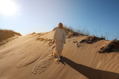 Man in arabic clothes walking through desert on sunny day