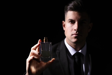 Man with luxury perfume against black background, focus on bottle