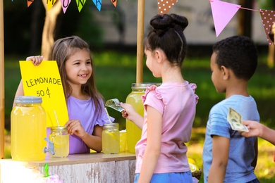 Little girl selling natural lemonade to kids in park. Summer refreshing drink