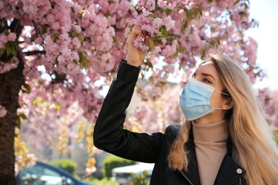 Woman with protective mask near blossoming tree outdoors. Seasonal pollen allergy