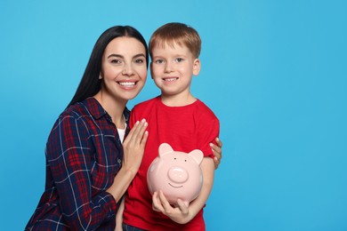 Mother and her son with ceramic piggy bank on light blue background