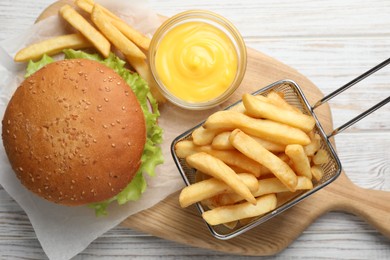 French fries in frying basket, tasty burger and sauce on white wooden table, flat lay