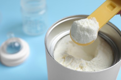 Scoop of powdered infant formula over can on light blue background, closeup. Baby milk