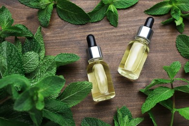Bottles of essential oil and mint on wooden table, flat lay