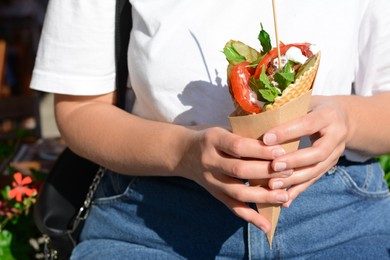 Photo of Woman holding wafer with falafel and vegetables outdoors, closeup. Street food