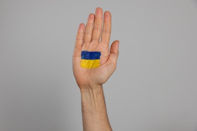 Man with drawing of Ukrainian flag on palm against light grey background, closeup