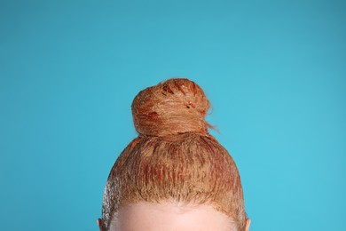Young woman dyeing her hair with henna on light blue background, closeup