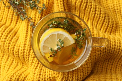 Photo of Fresh thyme tea with pieces of lemon on yellow knitted blanket, top view