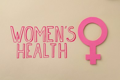 Female gender sign near text Women's Health on beige background, top view