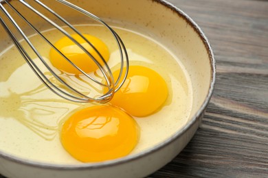 Whisking eggs in bowl on wooden table, closeup