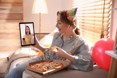 Woman with piece of pizza having online party via tablet at home during quarantine lockdown 
