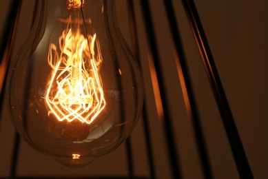 Photo of Hanging lamp bulb in chandelier against brown background, closeup