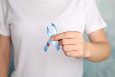 Woman holding light blue ribbon with paper blood drop on color background, closeup. World Diabetes Day