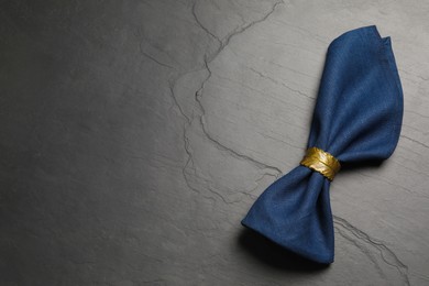 Blue fabric napkin with beautiful decorative ring on dark table, top view. Space for text