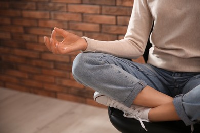 Woman meditating on chair near brick wall indoors, closeup