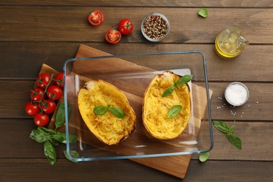 Halves of cooked spaghetti squash in baking dish and ingredients on wooden table, flat lay
