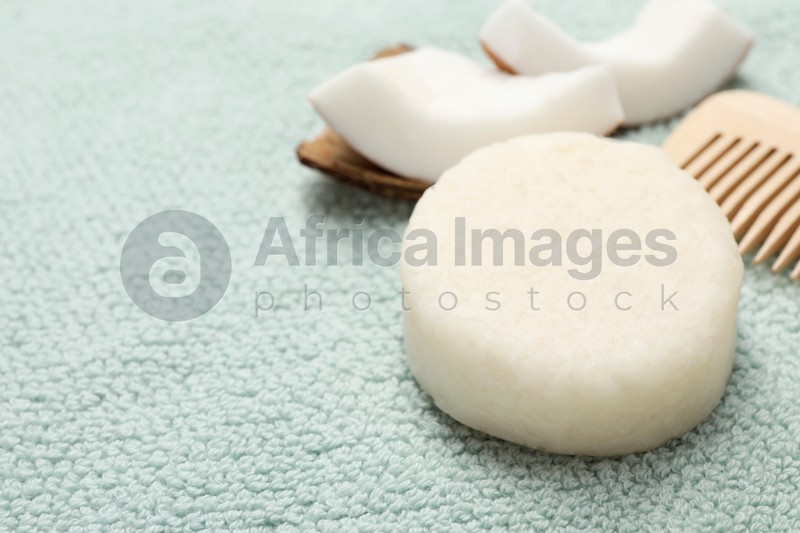 Photo of Solid shampoo bar, comb and coconut on light blue cloth, closeup. Space for text