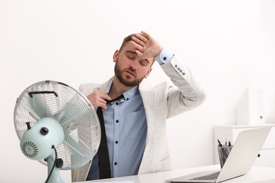 Man suffering from heat in front of fan at workplace