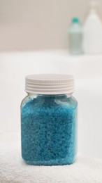 Jar with sea salt and fluffy towel on bath