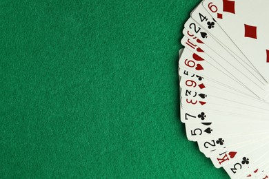 Fan of playing cards on green table, top view. Space for text