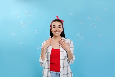 Photo of Young woman having fun with soap bubbles on light blue background