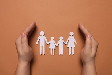 Man protecting paper family figures on brown background, top view. Insurance concept