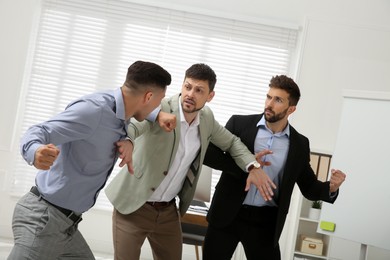 Photo of Man interrupting colleagues fight at work in office