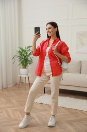 Young woman taking mirror selfie in stylish outfit at home. Morning routine