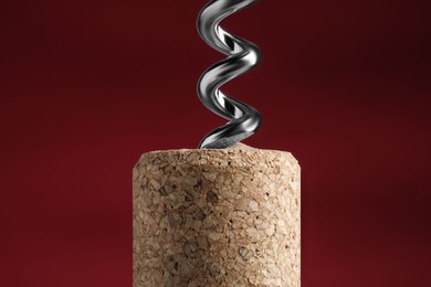 Photo of Corkscrew with cork against dark red background, closeup