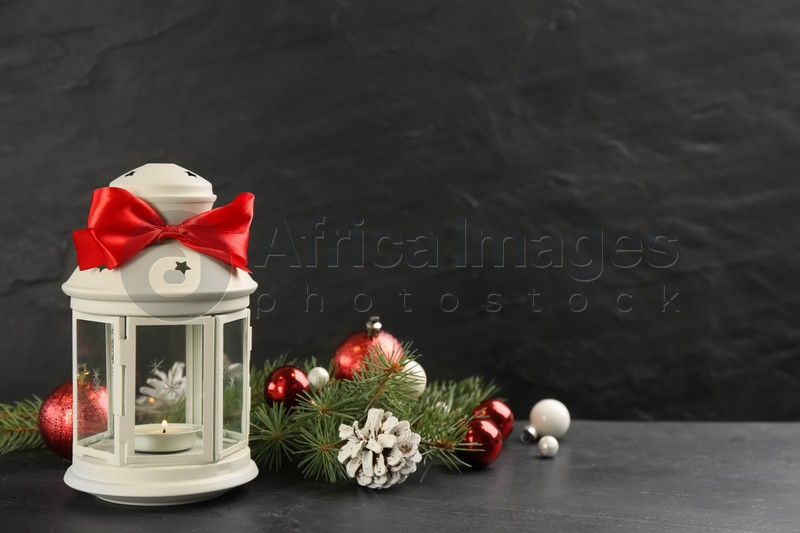 Photo of Christmas lantern with burning candle and festive decor on black background. Space for text