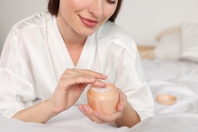 Woman taking hand cream from jar indoors, closeup