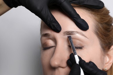 Beautician applying tint during eyebrows correction procedure on light grey background, closeup