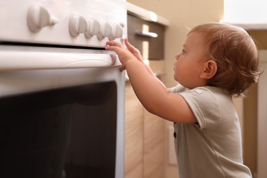 Little child playing with gas stove indoors. Dangers in kitchen