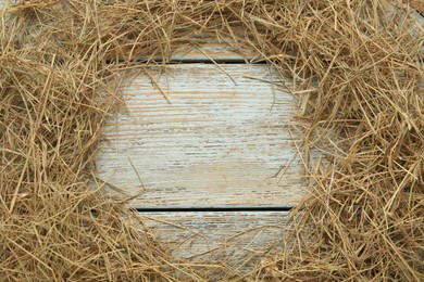 Frame of dried hay on light wooden background, flat lay. Space for text
