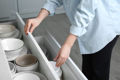 Photo of Woman opening drawers with plates and bowls in kitchen, closeup