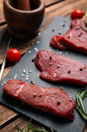 Fresh raw meat steaks and spices on wooden table, closeup
