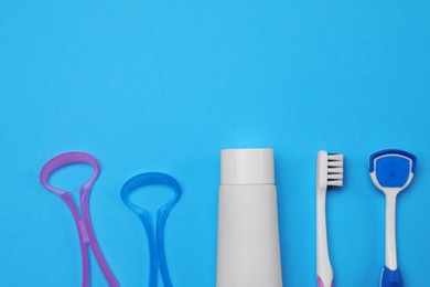Tongue cleaners, toothbrush and paste on blue background, flat lay. Space for text
