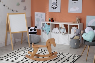 Photo of Wooden rocking horse and cute toys in playroom. Interior design