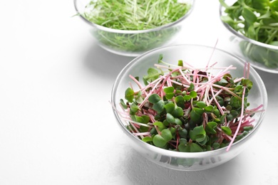 Glass bowl with fresh microgreen on white table, closeup. Space for text