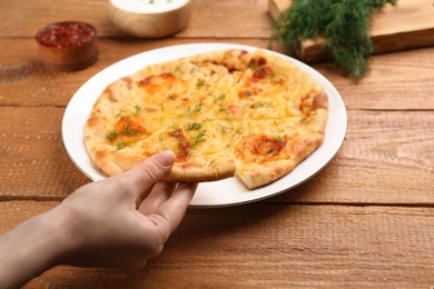 Woman taking piece of delicious khachapuri with cheese and dill at wooden table, closeup