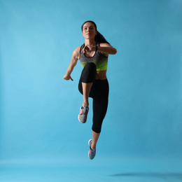 Athletic young woman running on light blue background