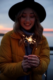 Photo of Woman in warm clothes holding burning sparkler outdoors